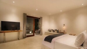 A modern hotel room with a large bed, a flat-screen TV, a seating area with a sofa and a small table, and a sliding glass door leading to a balcony. - 2 bedrooms Luxury Villa in Ubud with private pool (Gianyar Regency)