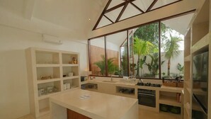 A modern kitchen with a central island, built-in shelves, and a large window offering a view of greenery. - 2 bedrooms Luxury Villa in Ubud with private pool (Gianyar Regency)