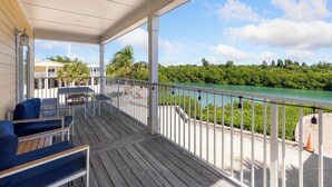 Eine Holzterrasse mit Gartenmöbeln, einem Geländer und Blick auf einen Fluss und Grünflächen.