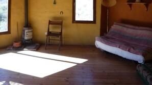 Quarto rústico com teto de madeira, uma cama, uma cadeira, uma mesa, luminária pendente e uma janela.
