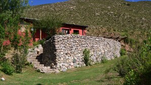 Mural de pedra com um edifício vermelho no topo, rodeado por vegetação e uma colina ao fundo.