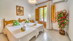 A hotel room with two beds, a large window with curtains, an air conditioning unit, and a potted plant with flowers. - House with pool Sirenas Playa de Muro (Playa de Muro)