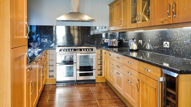 A modern kitchen with wooden cabinets, a stainless steel range hood, a built-in oven, and a granite countertop. - Conveniently located just 500 yards from the sandy beach. (Southerness, near Dumfries)
