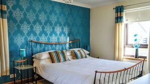 A neatly made bed with a wooden headboard, a bedside table with a lamp, and a window with curtains. - Conveniently located just 500 yards from the sandy beach. (Southerness, near Dumfries)