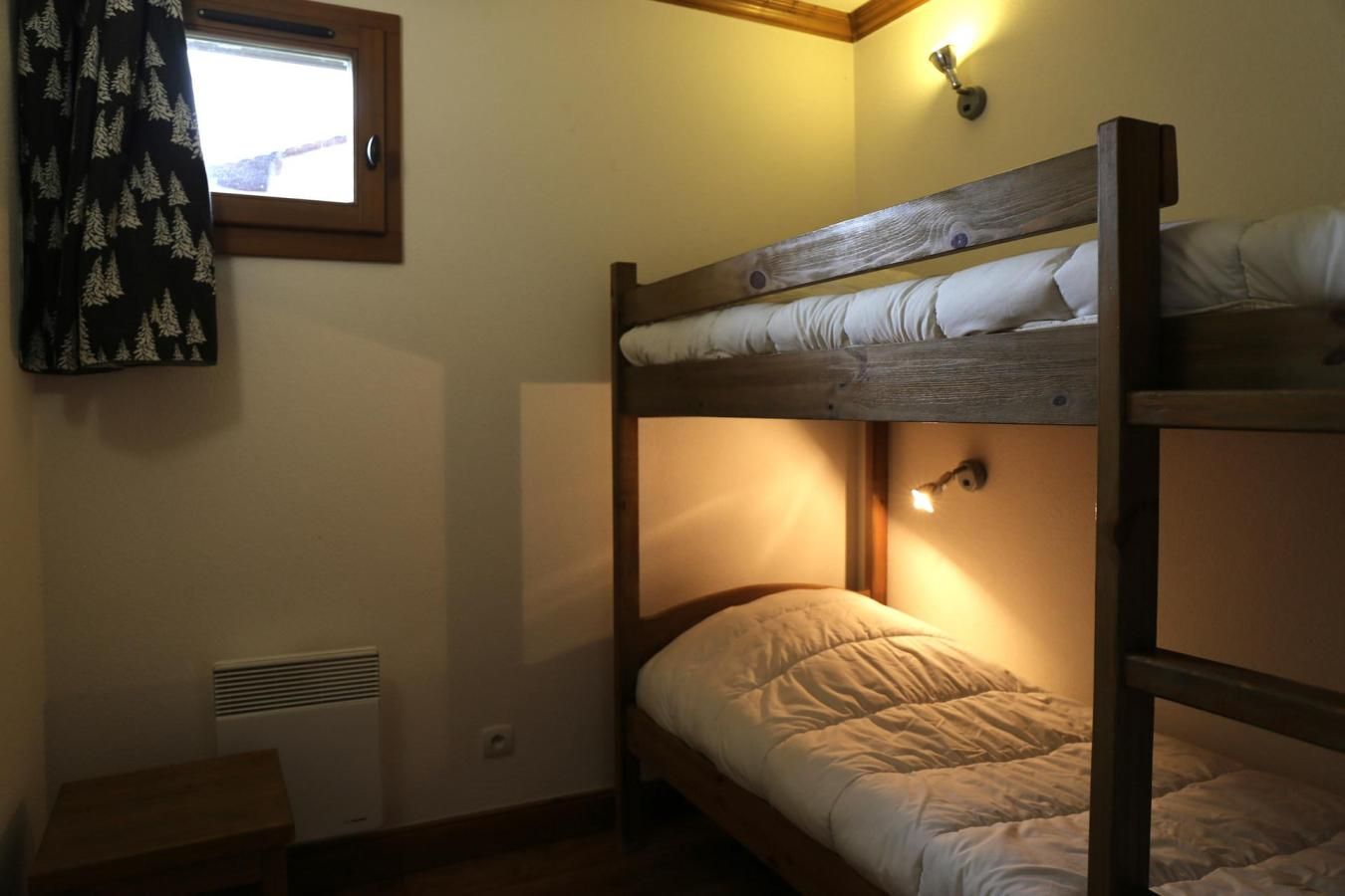 A bunk bed room with a window, a heater, and a small table.