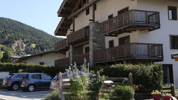 Un immeuble à plusieurs étages doté de balcons, entouré de verdure et ayant une chaîne de montagnes en toile de fond.