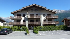 Un immeuble à deux étages doté de balcons, d’un parking et surplombant un paysage montagneux.