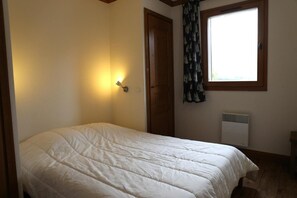 Une chambre à coucher avec un lit, une lampe fixée au mur, une fenêtre avec des rideaux et un radiateur.