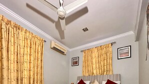 Ein Schlafzimmer mit einem Bett, Vorhängen, einem Deckenventilator, einer Klimaanlage und einem gerahmten Bild an der Wand.