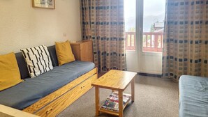 Een gezellige woonkamer met een bank, een houten tafel en een balkon met gordijnen met een patroon.