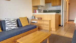 Een ruimtelijk ingerichte zithoek met een bank, een houten tafel en een kitchenette.