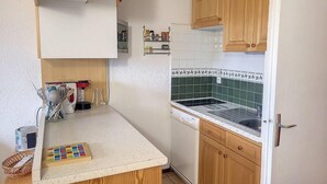 Een kleine keuken met houten kastjes, een wit aanrechtblad en een betegelde achterwand.