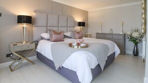 A modern bedroom with a large bed, bedside tables, a dresser, and decorative items. - Closefield (Leighton Buzzard)