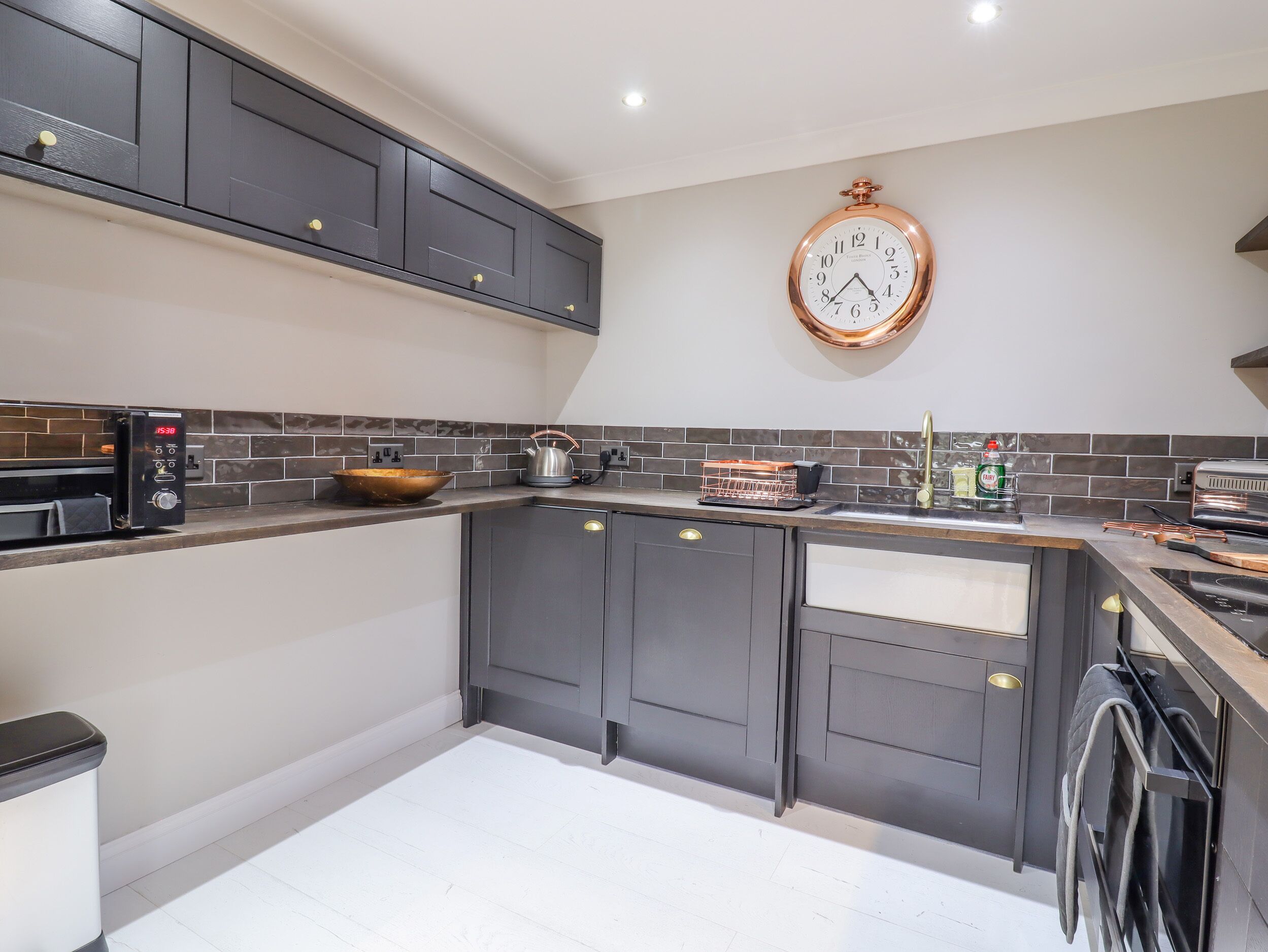 A modern kitchen with dark cabinets, a stainless steel toaster, a kettle, and a clock on the wall.