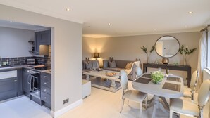 A modern kitchen with integrated appliances, a dining area with a round table and chairs, and a cozy seating area with a sofa and cushions. - Closefield (Leighton Buzzard)