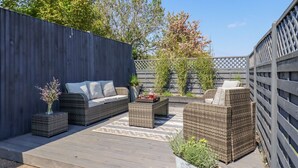 A patio with wicker furniture, a wooden deck, and a garden bed with plants. - Closefield (Leighton Buzzard)
