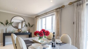 A dining area with a round table set for two, a vase with red flowers, and a bottle of champagne. - Closefield (Leighton Buzzard)