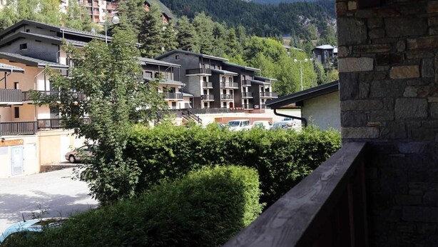 Un edificio de varios pisos con balcones, rodeado de abundante vegetación y montañas al fondo.