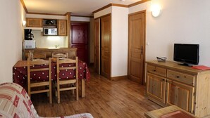 Una habitación compacta con una mesa de comedor de madera, sillas, televisor y una pequeña cocina.