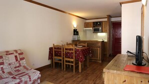 Un espacio habitable compacto con comedor, kitchenette y televisor sobre una mesa de madera.