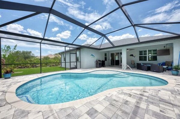 A swimming pool with a glass enclosure, a patio area with outdoor furniture, and a view of the surrounding landscape.