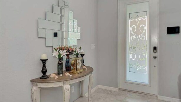 Un couloir avec une porte blanche, un miroir et une console ornée d’objets décoratifs.
