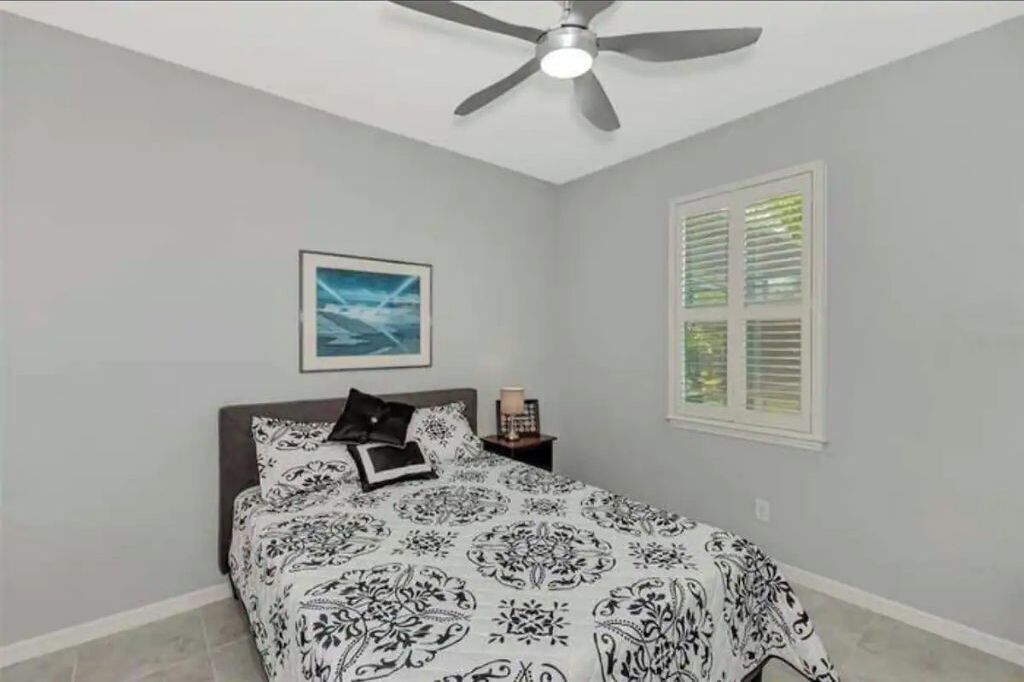 A bedroom with a bed, a ceiling fan, a window with blinds, and a framed picture on the wall.
