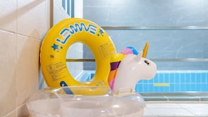 A yellow inflatable ring with 'LEWAVE' written on it, a white unicorn float, and a clear glass window with a pool in the background.