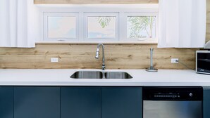 A modern kitchen with a stainless steel sink, a dishwasher, and a window with three framed pictures. - Turibana 50 G (Noord)