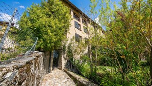 A stone pathway leading to a building with a rustic facade, surrounded by greenery and a clear blue sky. - Casa Dell'antonio With Sauna (Aranno)
