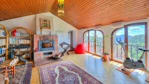 A spacious living area with a fireplace, bookshelves, a chessboard, a large rug, and a view of the outdoors. - Casa Dell'antonio With Sauna (Aranno)