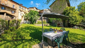 A patio with a table and chairs, surrounded by a well-maintained lawn and stone walls. - Casa Dell'antonio With Sauna (Aranno)