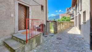 A narrow stone-paved alleyway with a red metal gate, a door with a herringbone pattern, and a stone wall. - Casa Dell'antonio With Sauna (Aranno)