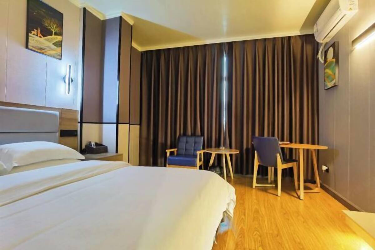 Et hotelværelse med en seng, to stole, et lille bord, et billede på væggen og en aircondition.