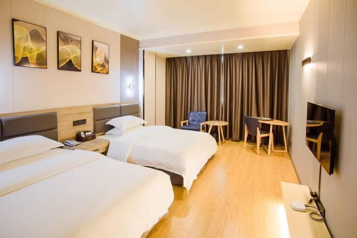 Et hotelværelse med to senge, et skrivebord, en stol, et fjernsyn og et gardin.