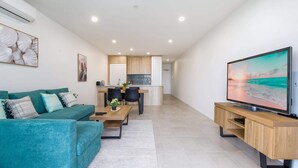A modern living room with a teal sofa, a coffee table, and a TV on a wooden stand. - Stunning 1-Bed Bayside Apartment with Superb Views (Batemans Bay)