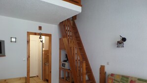 A room with a wooden staircase, a bed with a patterned bedspread, a wooden cabinet, and a small table. - FOUX D'ALLOS MEZZANINE STUDIO 28M2 (foux d'allos)