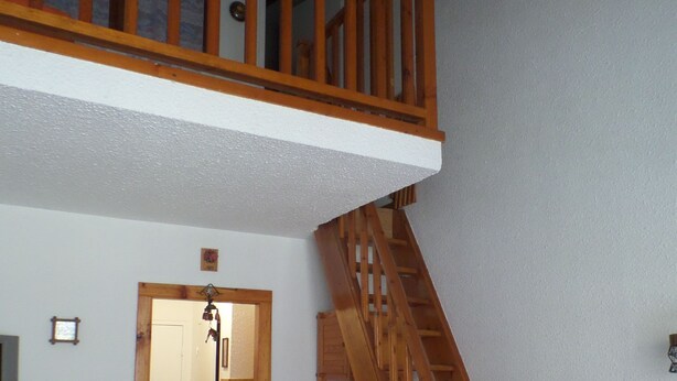 A room with a wooden staircase leading to an upper level, a door, and a microwave on a shelf. - FOUX D'ALLOS MEZZANINE STUDIO 28M2 (foux d'allos)