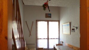 A room with a wooden staircase, a sofa, a dining table with chairs, a window with curtains, and a wall-mounted picture. - FOUX D'ALLOS MEZZANINE STUDIO 28M2 (foux d'allos)