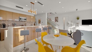 Une cuisine moderne dotée d’un îlot central, de tabourets de bar et d’une table à manger avec des chaises jaunes.