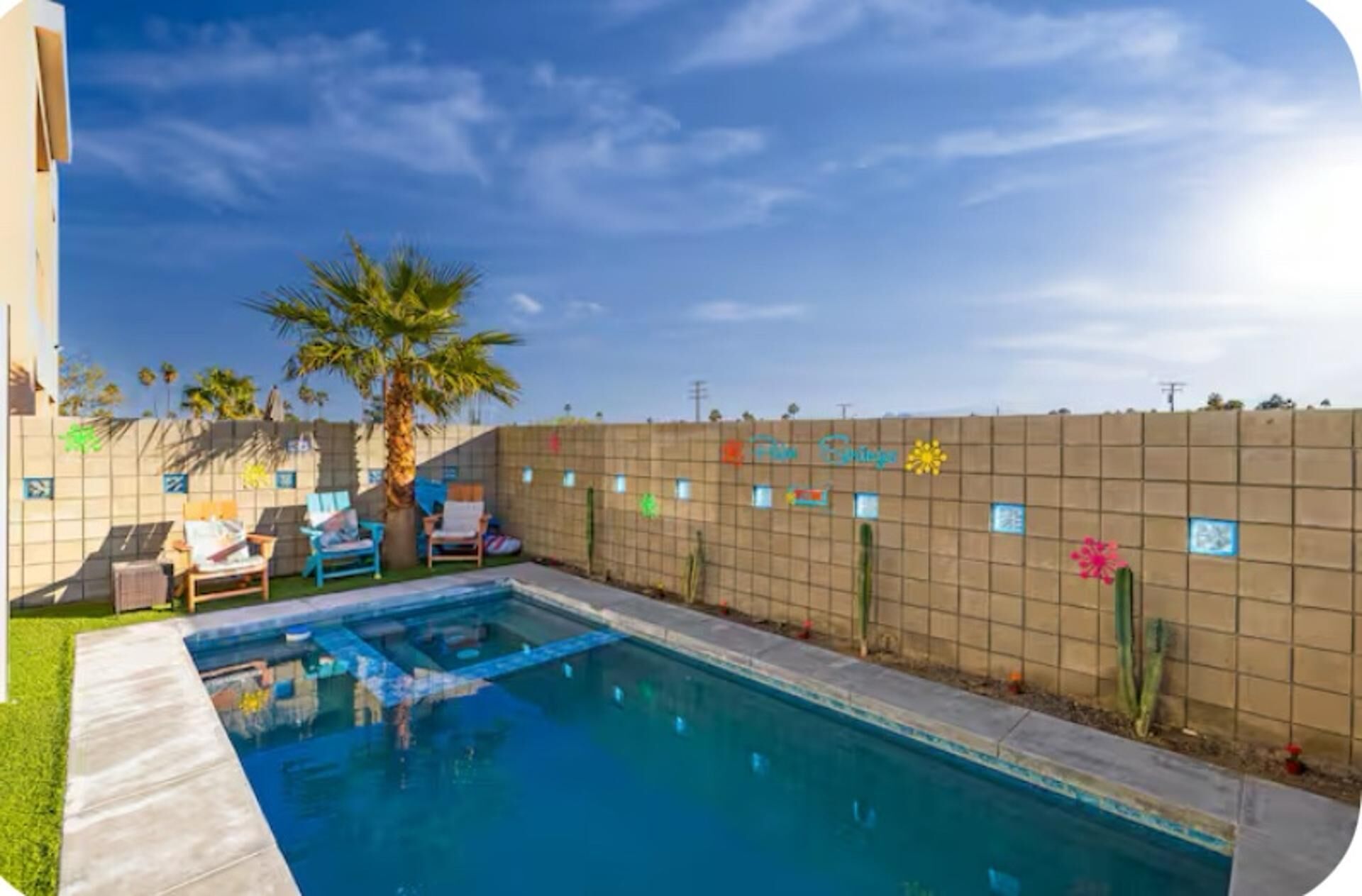 A swimming pool with a tiled wall, palm trees, and lounge chairs.