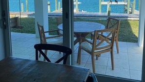A view from a room with a sliding glass door to a patio area with a round table and chairs, overlooking a body of water and a dock. - 3 BR sleeps 10 WATER FRONT w BOAT SLIP + FABULOUS POOL  (Treasure Cay)