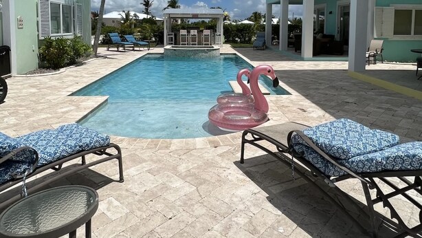 A pool area with lounge chairs, a decorative flamingo float, and a clear blue sky. - 3 BR sleeps 10 WATER FRONT w BOAT SLIP + FABULOUS POOL  (Treasure Cay)