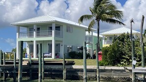 A two-story house with a balcony, located near a body of water with wooden pilings. - 3 BR sleeps 10 WATER FRONT w BOAT SLIP + FABULOUS POOL  (Treasure Cay)