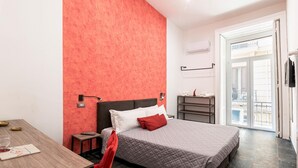 Et hotelværelse med seng, skrivebord, stol, natbord og garderobeskab.