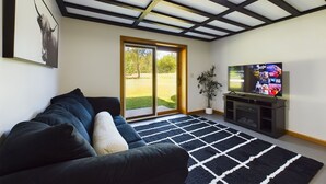 A modern living room with a large sofa, a flat-screen TV, and a view of a grassy area through a sliding glass door.