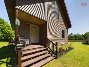 A two-story house with a wooden deck, a front door, and a small porch area with a chair and table.