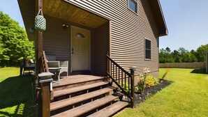 A two-story house with a wooden deck, a front door, and a small porch area with a chair and table.