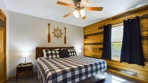 A bedroom with a bed, a ceiling fan, a wall clock, and a window with curtains.