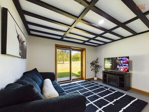 A modern living room with a large sofa, a flat-screen TV, and a view of a grassy area through a sliding glass door.
